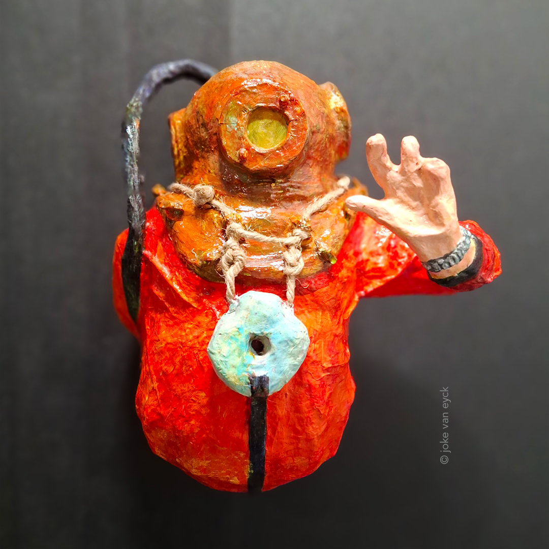 Deep-sea diver waving 1 arm. Wears copper helmet with 3 portholes, front one closed with window, the other, at level of ears with bars. Man is solidly built with thick belly, wears red suit with heavy weight on chest. weight hangs with heavy rope around helmet. Waving hand has only 3 fingers and wears wristwatch (omega seamaster). From helmet comes black oxygen tube at back. Painted sculpture, recycled paper pulp, painted.